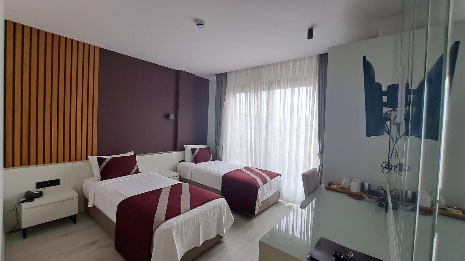 A hotel room with two beds, a desk, a chair, and a glass partition.