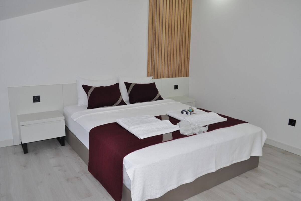 A modern bedroom with a bed, white nightstands, and a wooden panel wall.