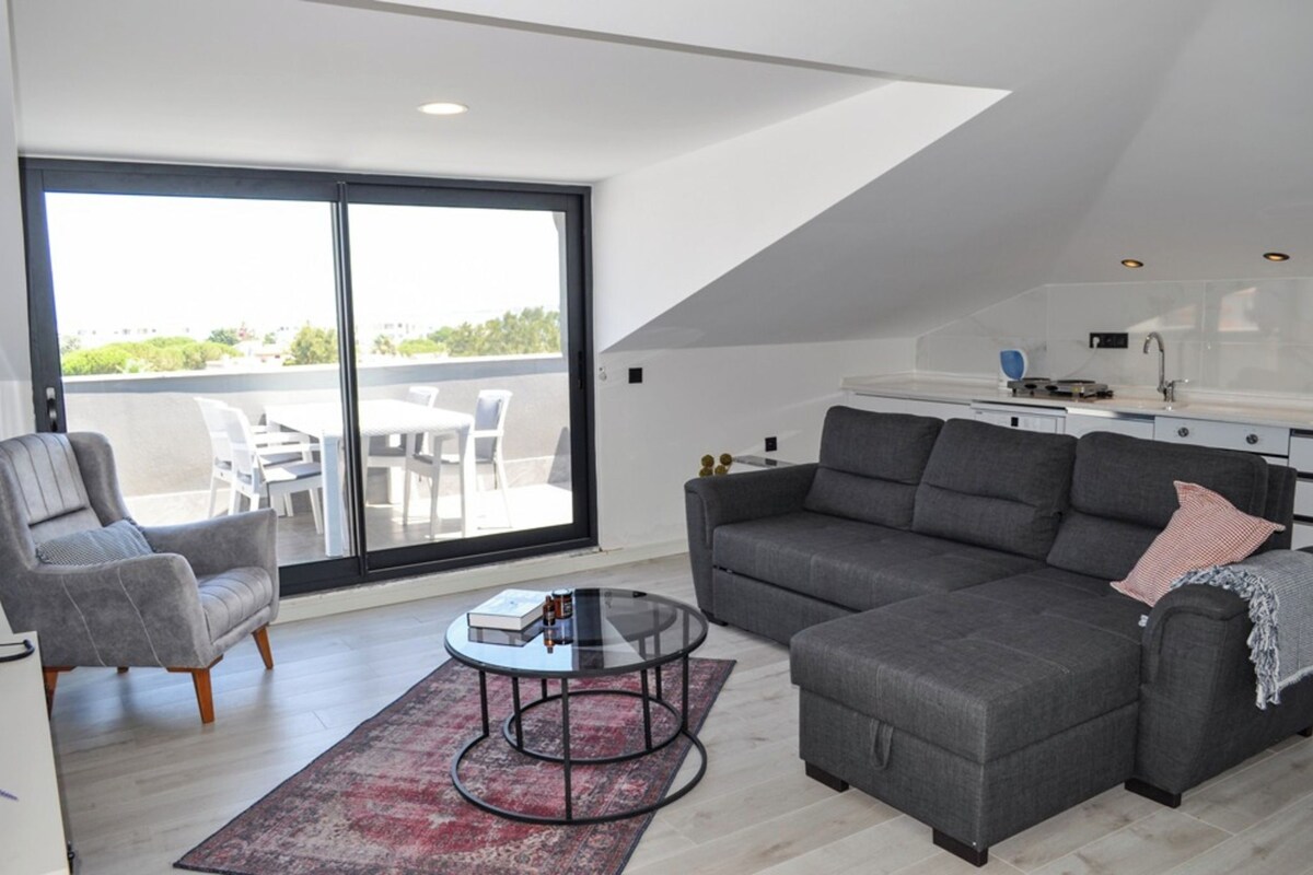 A modern living room with a grey sofa, a glass coffee table, and a dining area with a white table and chairs.