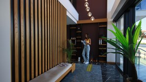 Un interior moderno con un revestimiento de listones de madera, un banco, una planta en maceta y una persona de pie cerca de una puerta.