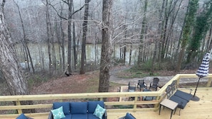 A deck with outdoor furniture, a view of a forest, and a body of water in the background. - Hidden Lake Sanctuary  (West Union)