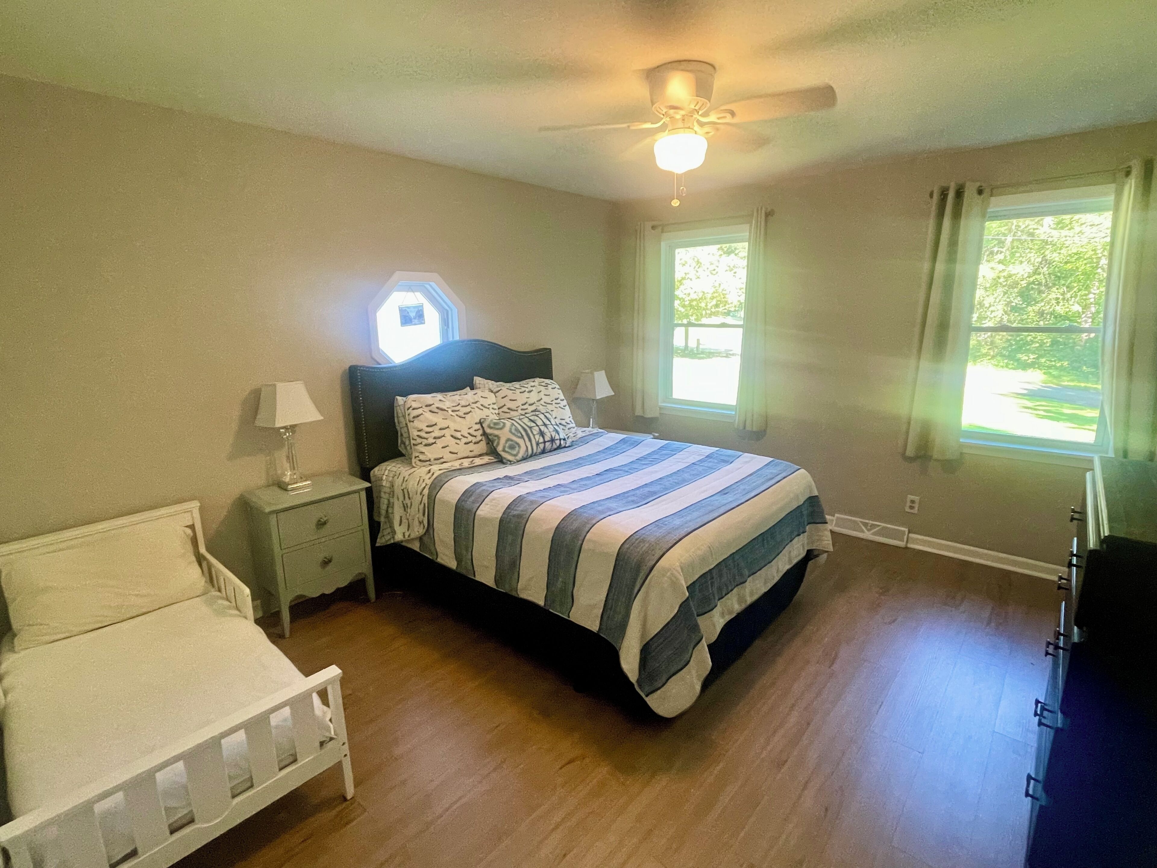 A bedroom with a bed, nightstands, a ceiling fan, and two windows with curtains.