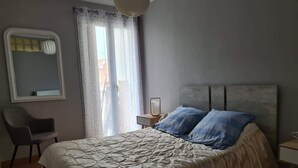 A bedroom with a bed, a chair, a nightstand, and a window with curtains. - Charming accommodation on the port of Mèze (Mèze)