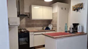 A compact kitchen with white cabinets, a stove, a sink, and a coffee maker. - Charming accommodation on the port of Mèze (Mèze)