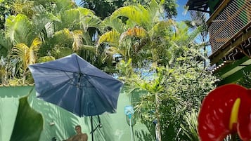 Uma área de piscina com um guarda-sol azul, rodeada por vegetação exuberante e vista para uma paisagem tropical.