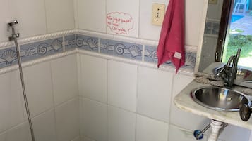 A bathroom with white tiles, a blue and white patterned border, a toilet, a sink with a faucet, and a shower head.