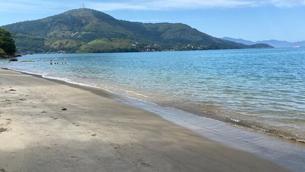 Une plage à l’eau claire, un rivage sablonneux et une montagne en arrière-plan.