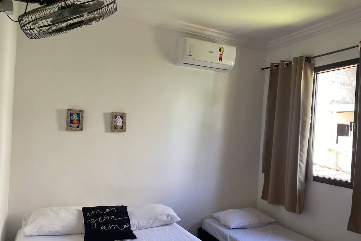 Un dormitorio con dos camas individuales, aire acondicionado de pared y una ventana con cortinas.