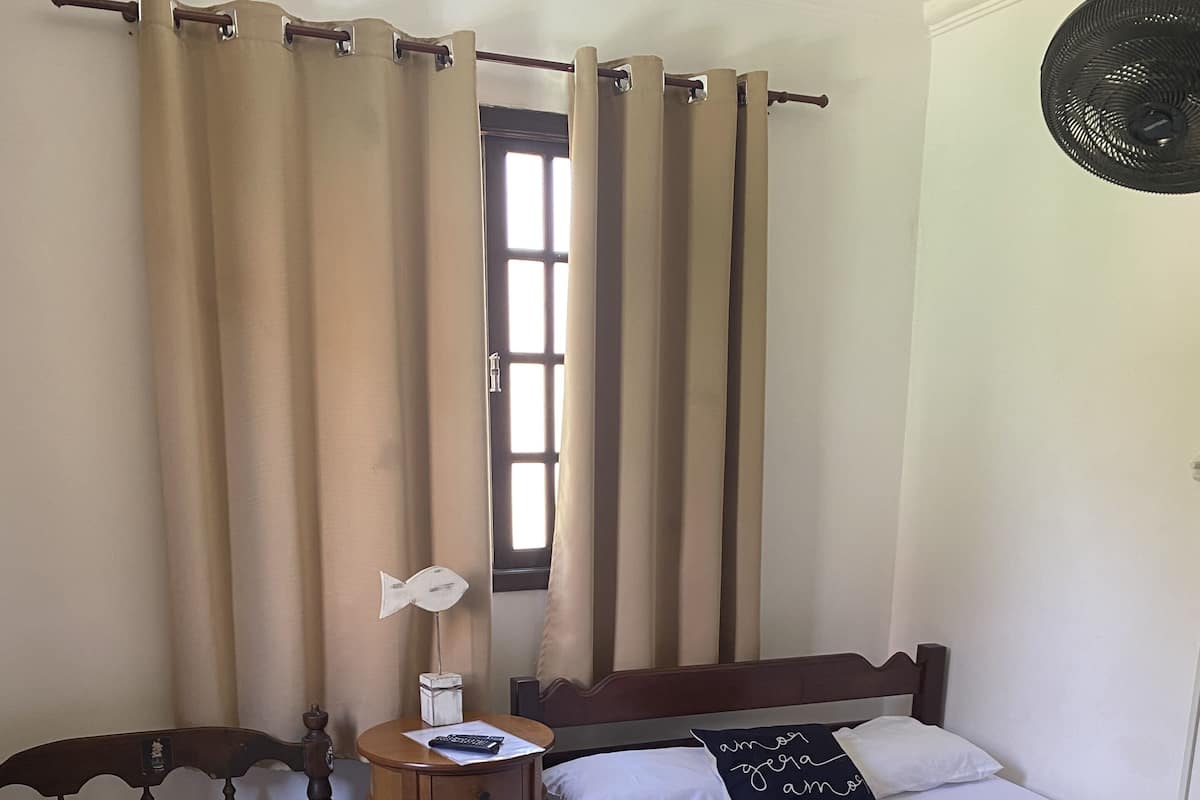 Un dormitorio con dos camas individuales, una mesita de noche con lámpara y una ventana con cortinas.