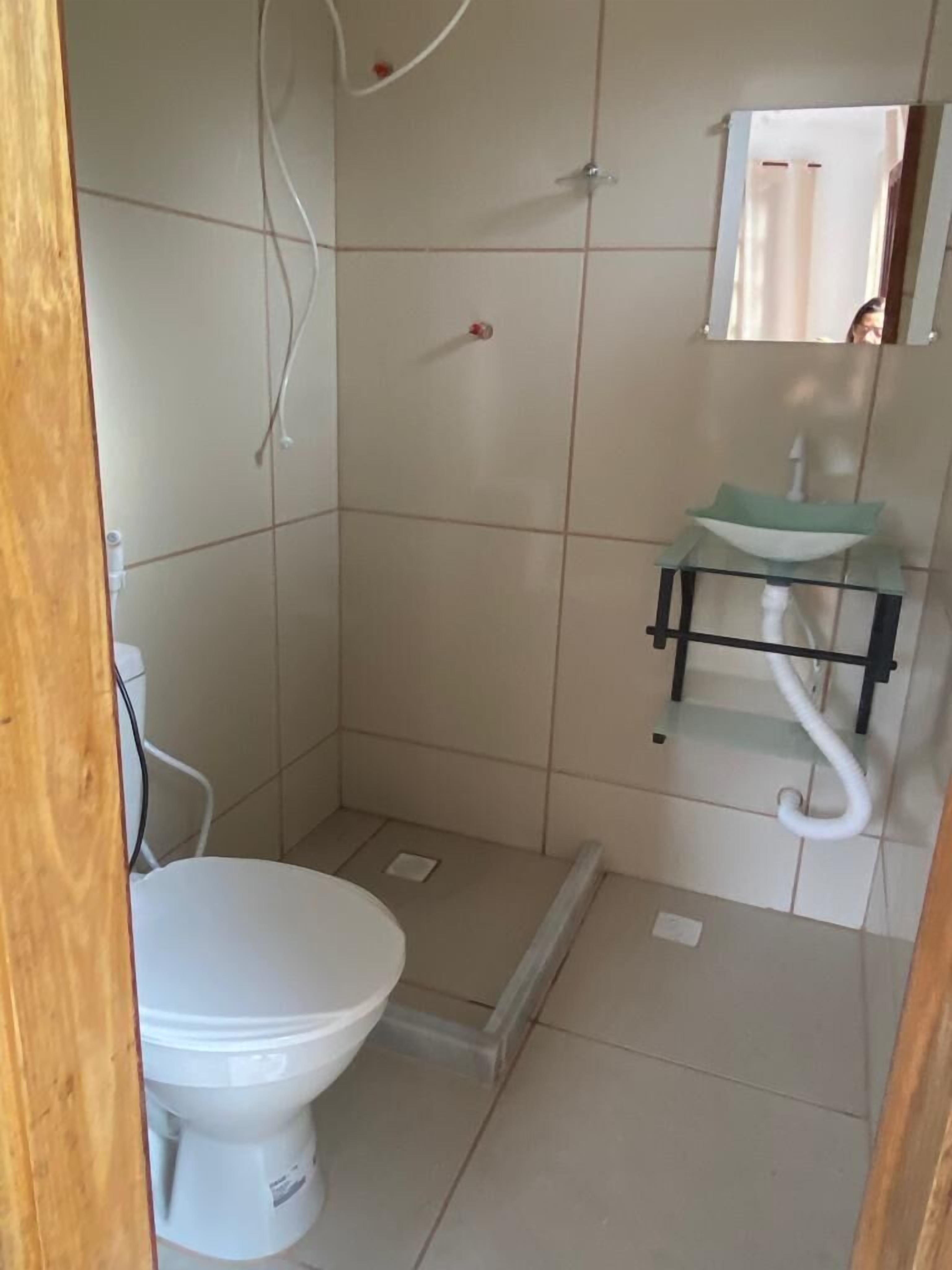 A small, tiled bathroom with a white toilet, a glass sink on a black stand, and a mirror above the sink.