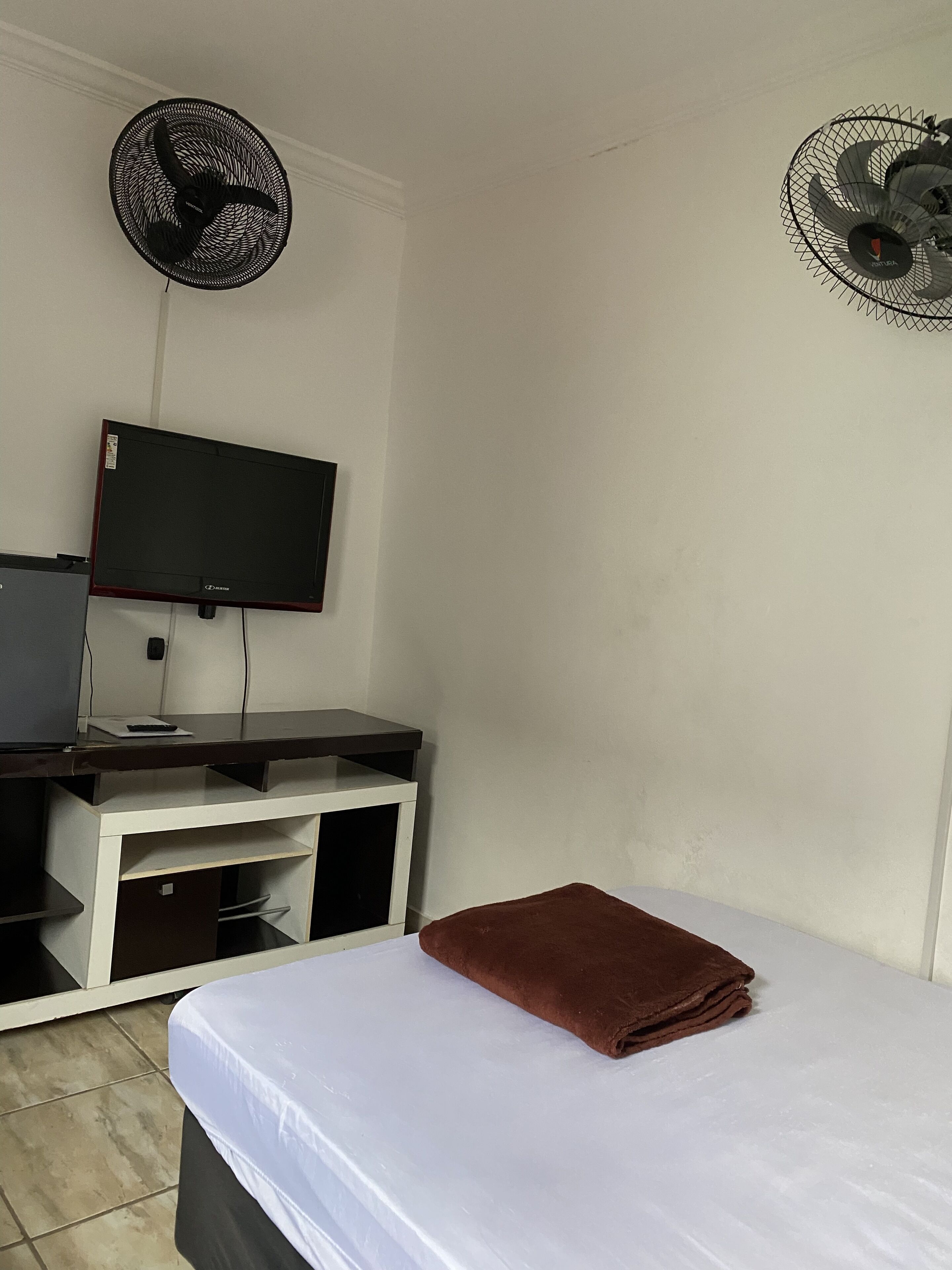 A room with a bed, a TV on a stand, and two wall fans.