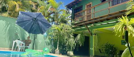 A swimming pool with a green inflatable float, a blue umbrella, and a chair.