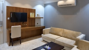 Una sala de estar moderna con un escritorio de madera, un sofá color beige, un televisor y un equipo de aire acondicionado.