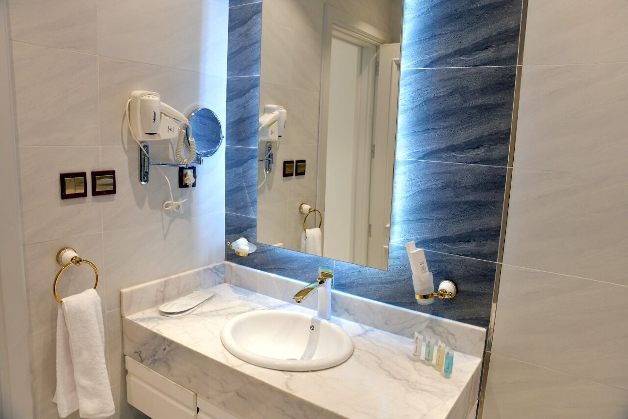 A bathroom with a marble sink, a large mirror, and a hairdryer mounted on the wall.