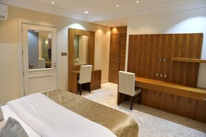 Habitación de hotel con cama, escritorio, silla, armario y espejo.