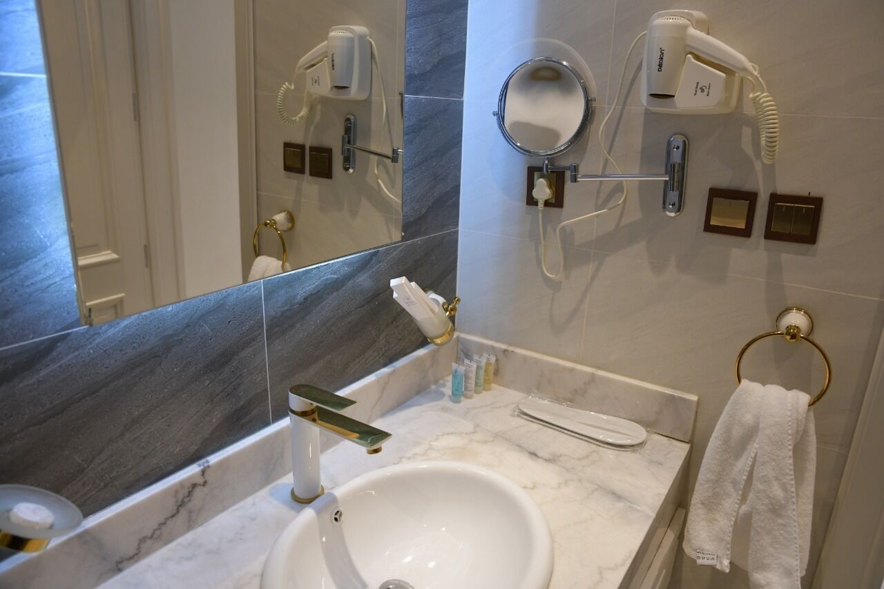 A bathroom with a white sink, a mirror, a towel ring, and two hair dryers mounted on the wall.