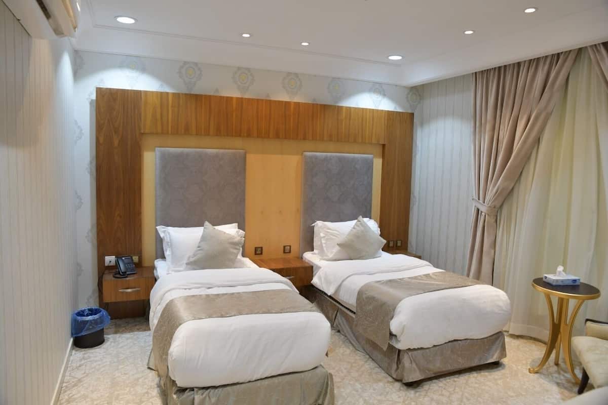A hotel room with two beds, a wooden headboard, a small bedside table with a phone, a blue trash bin, and a round side table with a tissue box.