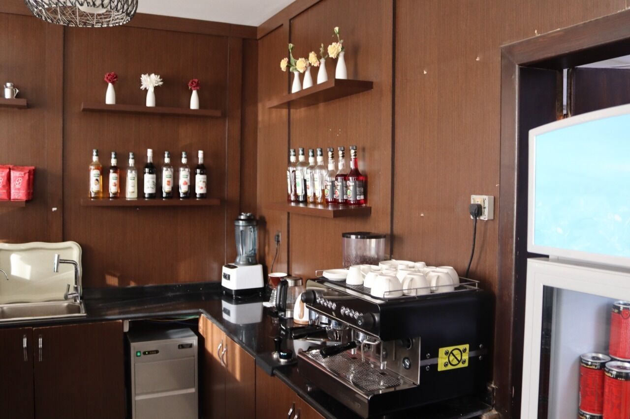 A kitchen with a coffee machine, shelves with bottles, and a refrigerator.