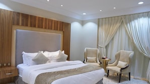 Habitación de hotel con una cama grande, dos sillones, una mesita auxiliar y un cabecero de madera.