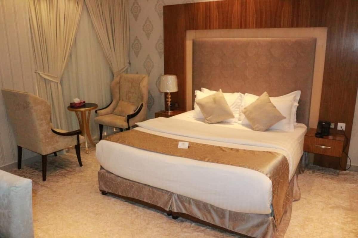 A hotel room with a large bed, a chair, a small table, and a nightstand.