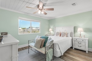 A bedroom with a bed, bedside tables, a desk, a chair, a ceiling fan, and a window with a view of buildings. - Renovated Gulf front corner unit w/panoramic views | Beach access w/free setup (Seagrove Beach)