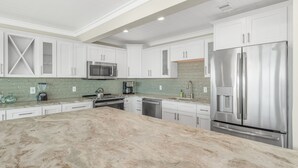 A modern kitchen with white cabinetry, stainless steel appliances, and a marble countertop.