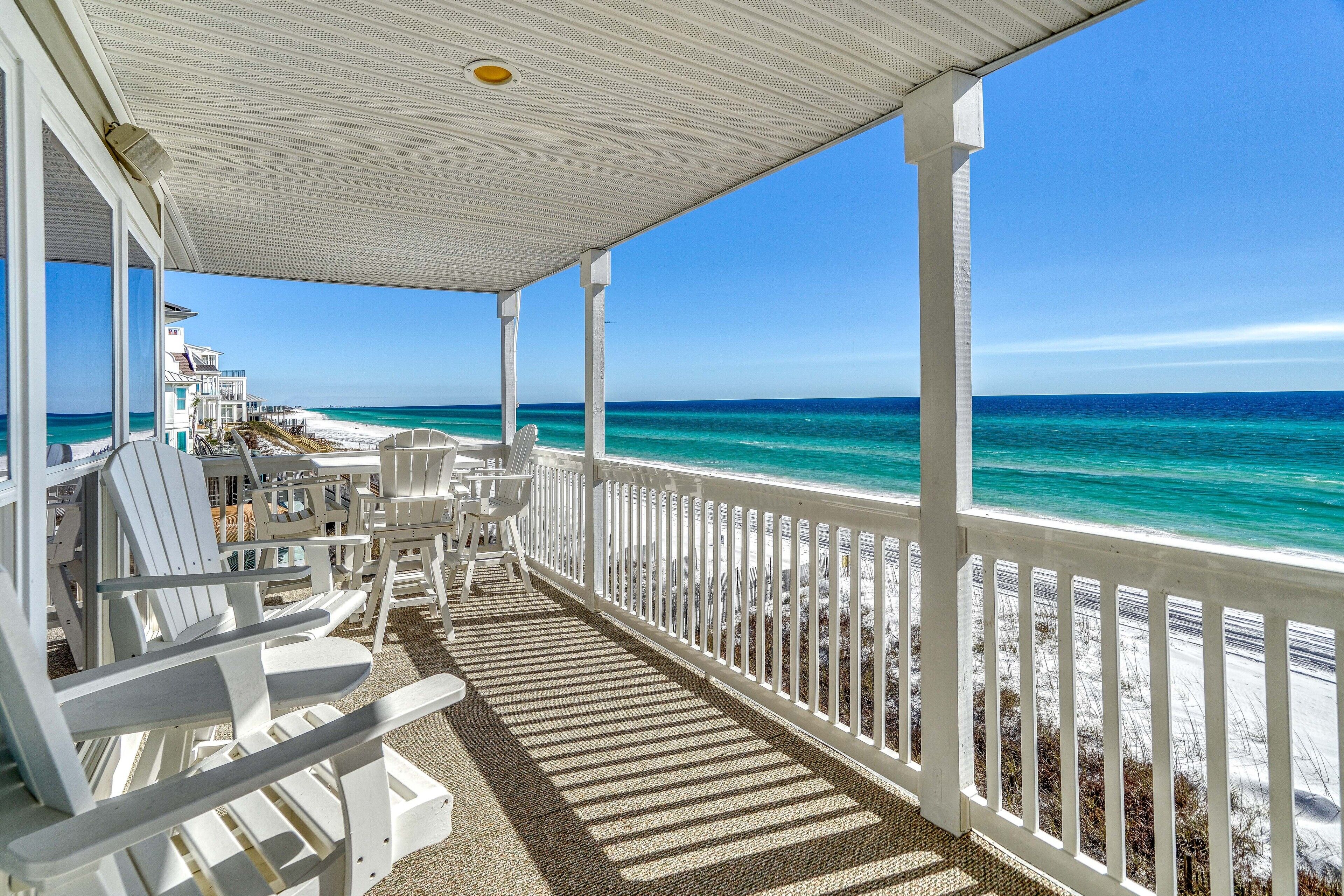 A covered outdoor area with white chairs and a view of the beach.