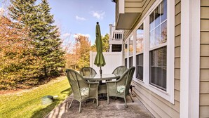 Eine Terrasse mit Tisch und Stühlen, einem Sonnenschirm und Blick auf ein Haus mit Zaun und Bäumen.
