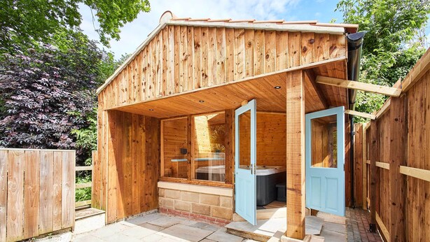 A wooden structure with a door open, a window, and a small outdoor area with steps leading to a hot tub. - Host & Stay | Littlebeck House (Whitby)