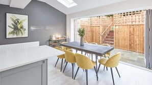 A modern dining area with a table and chairs, a radiator, a plant, and a view of a wooden fence and stairs. - Host & Stay | Littlebeck House (Whitby)