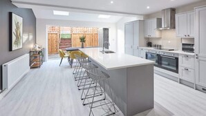 A modern kitchen with a central island, bar stools, and a view of a wooden deck. - Host & Stay | Littlebeck House (Whitby)