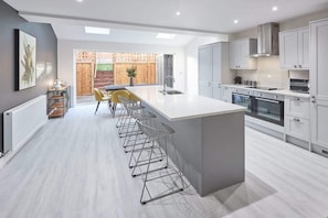 A modern kitchen with a central island, bar stools, and a view of a wooden deck. - Host & Stay | Littlebeck House (Whitby)