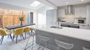 A modern kitchen with a large island, bar stools, and a view of a wooden fence. - Host & Stay | Littlebeck House (Whitby)