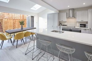 A modern kitchen with a large island, bar stools, and a view of a wooden fence. - Host & Stay | Littlebeck House (Whitby)