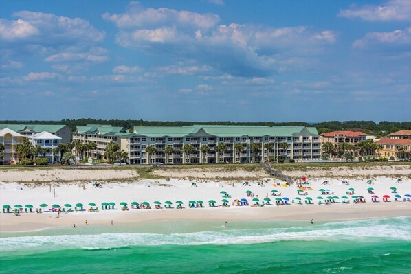 A beachfront hotel with multiple buildings, a sandy beach, and umbrellas.