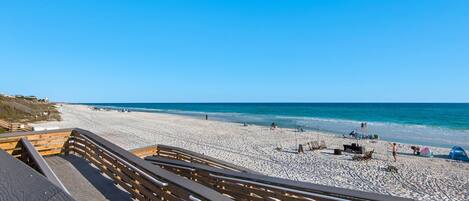 A beach with a wooden boardwalk leading to the shore, sandy beach, and the ocean.