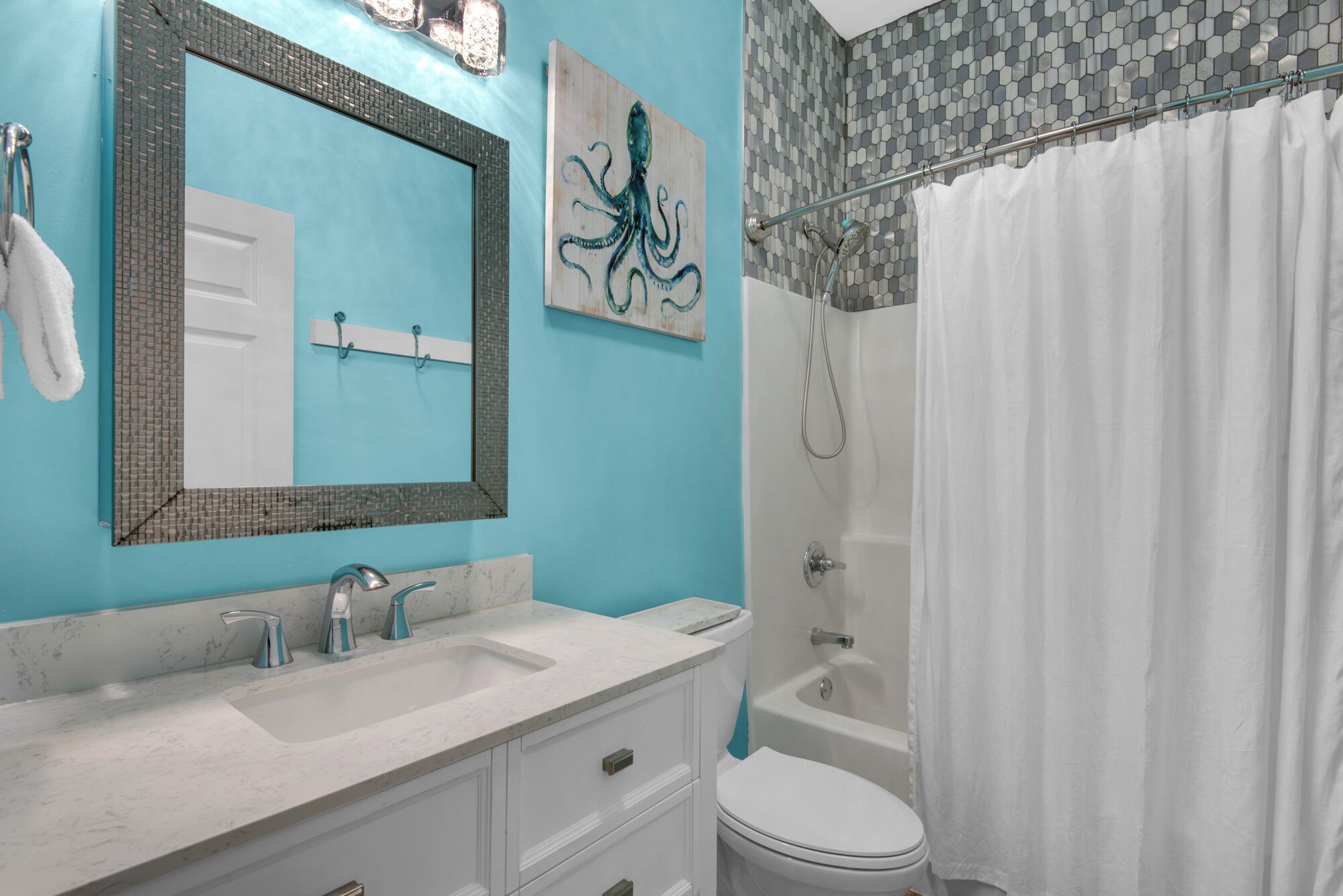 A bathroom with a blue wall, a white sink with a marble countertop, a white toilet, and a shower with a glass door.