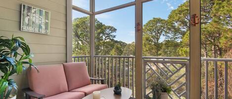 A balcony with a cushioned seating area, a small table, and potted plants.