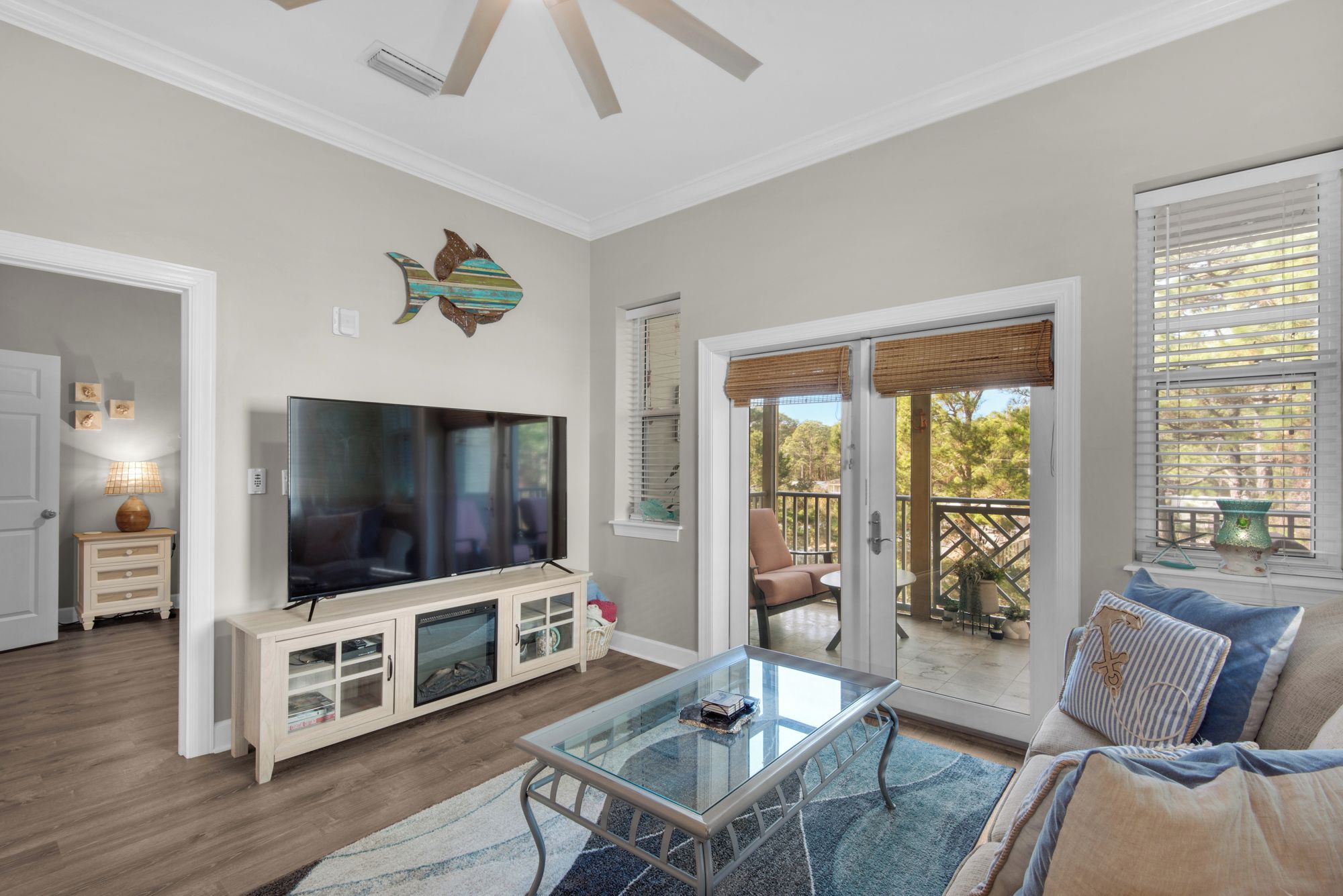 A living room with a flat-screen TV, a glass coffee table, a sofa, and a sliding glass door leading to an outdoor patio.