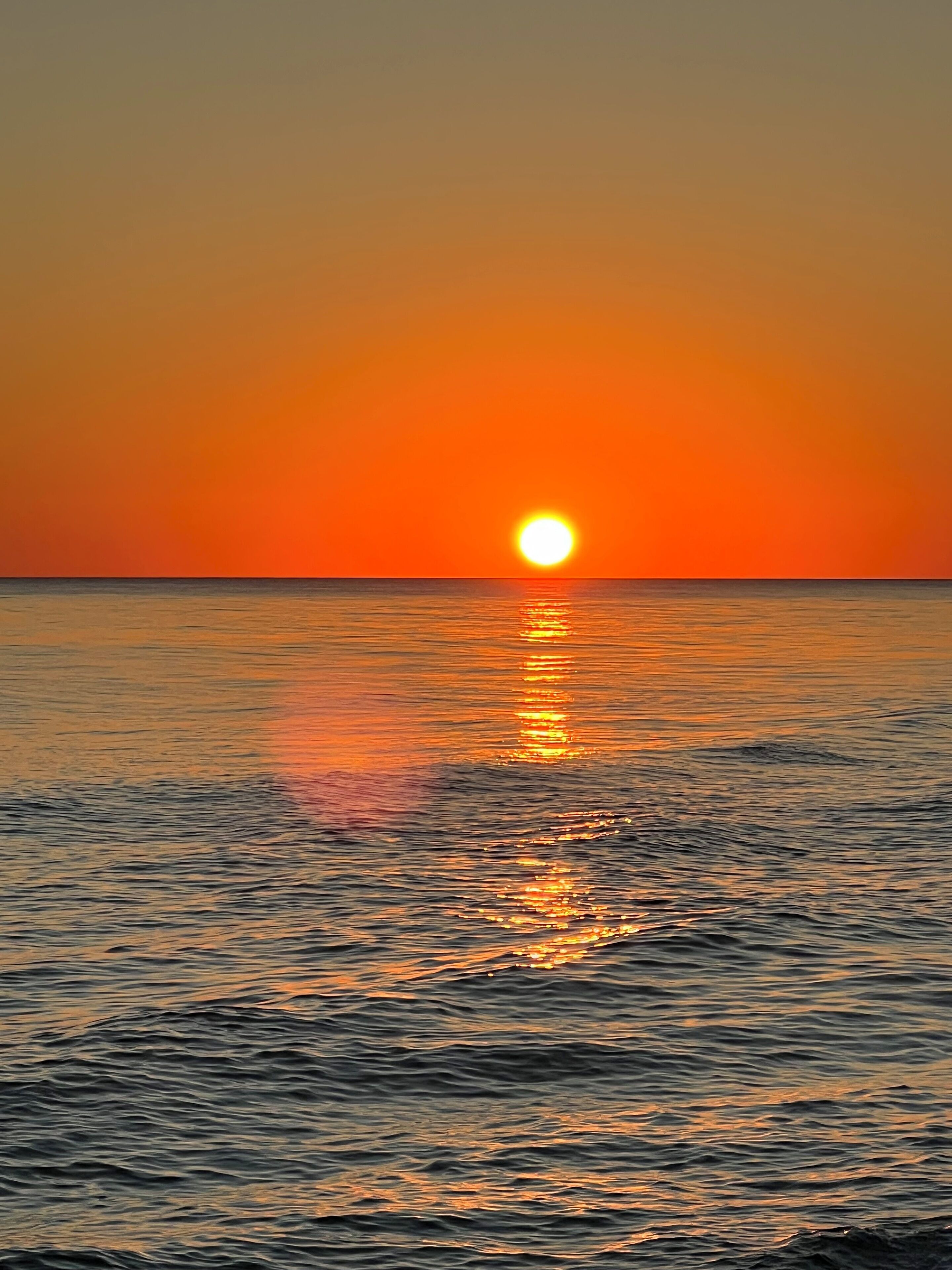 Un coucher de soleil sur une mer calme, le soleil se reflétant sur l’eau.