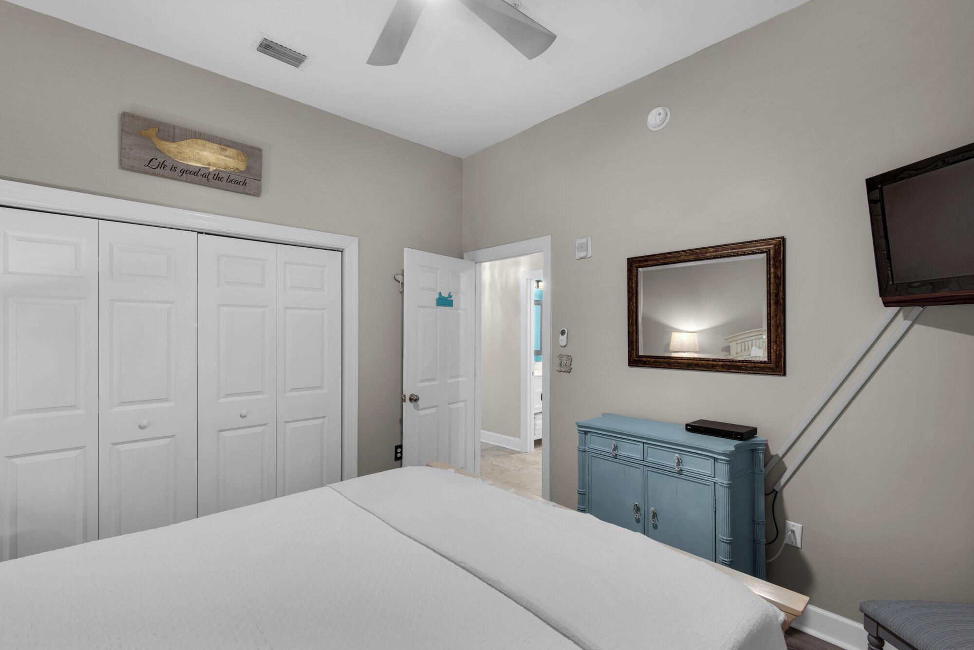 Une chambre à coucher comprenant un lit, une commode, un miroir et un ventilateur de plafond.