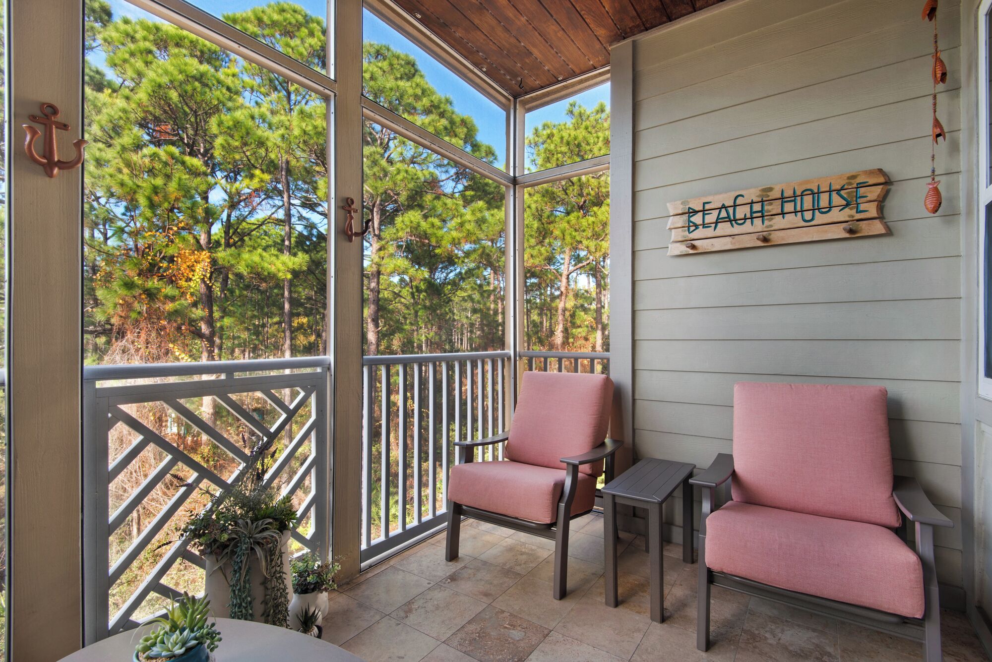 A covered patio with two pink chairs and a small table, overlooking a forested area.