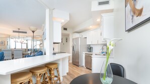 Una cocina moderna con armarios blancos, un refrigerador de acero inoxidable y un comedor con sillas de mimbre y una mesa negra.