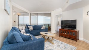 Una sala de estar con un sofá azul, una mesita redonda y un televisor sobre un mueble de madera.