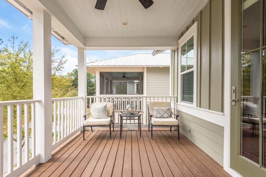 Eine überdachte Veranda mit Holzdeck, weißen Geländern und zwei Stühlen mit Kissen.