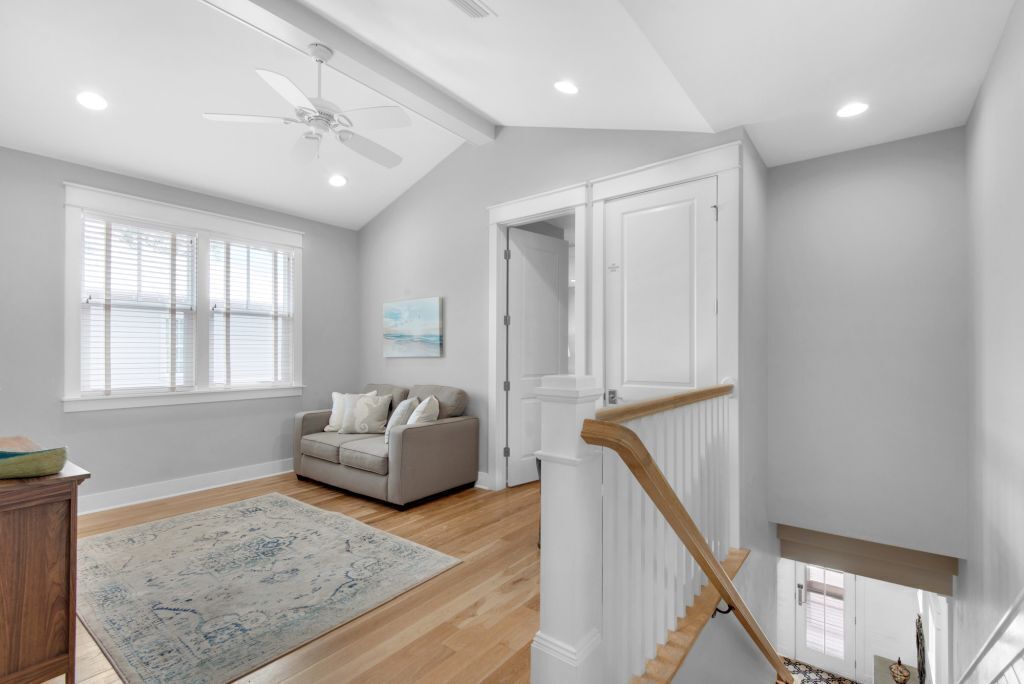 Un salon spacieux avec un plafond haut, un ventilateur de plafond, un canapé gris, un plancher en bois et une vue sur un escalier.