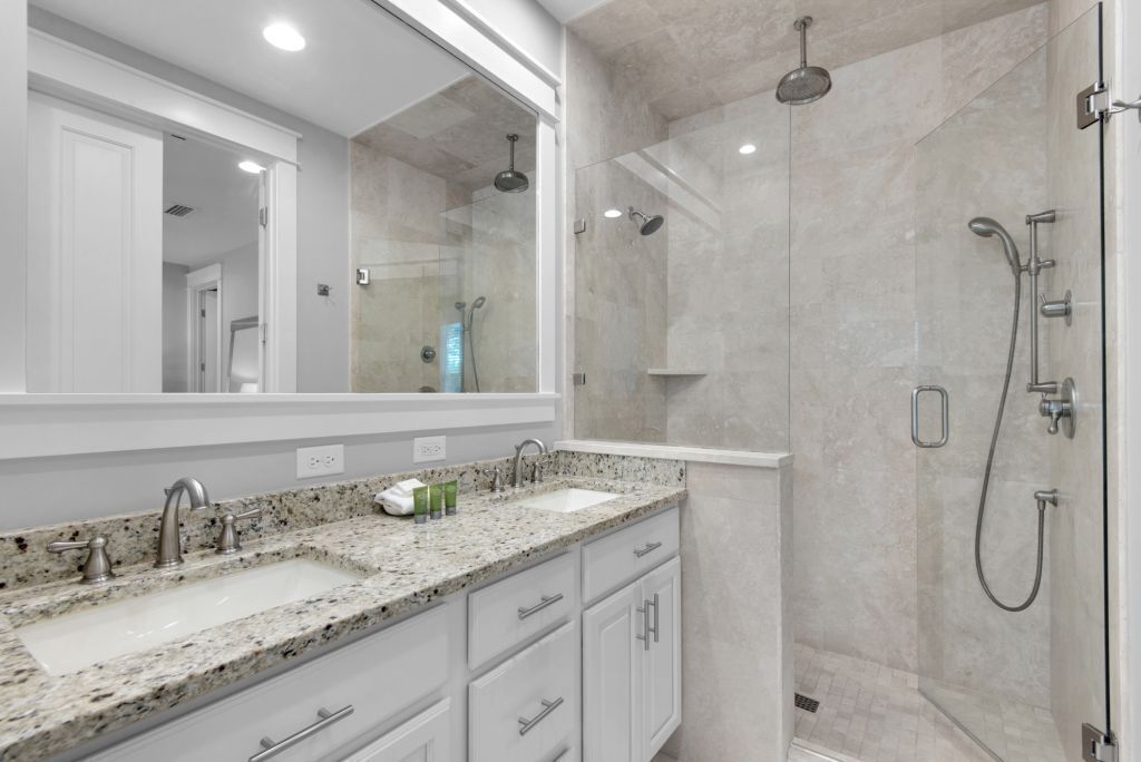 A modern bathroom with a large mirror, two sinks, and a walk-in shower.