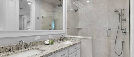 A modern bathroom with a large mirror, two sinks, and a walk-in shower.