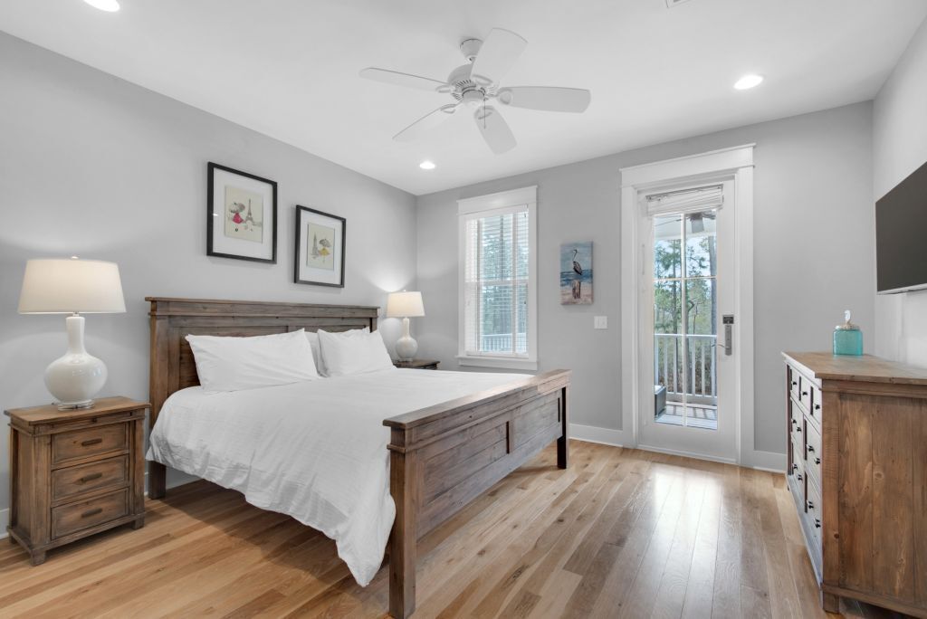 A bedroom with a wooden bed, two bedside tables with lamps, a ceiling fan, and a door leading to a balcony.