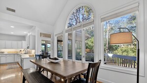 Une cuisine spacieuse dotée d’une grande table à manger, de meubles blancs et offrant une vue sur l’extérieur grâce à de grandes fenêtres.